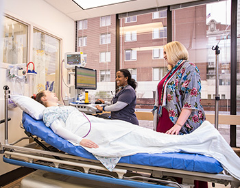 Hospital room with two care providers having a discussion with a patient lying in a bed.