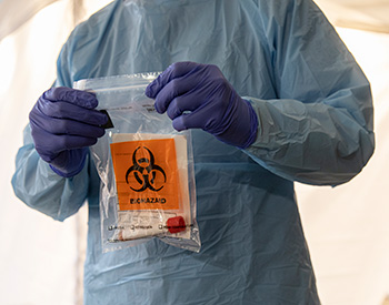 A gowned and gloved individual holding a biohazard bag.