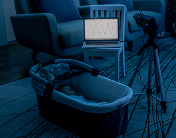 A bassinet, laptop and camera in a darkened room.